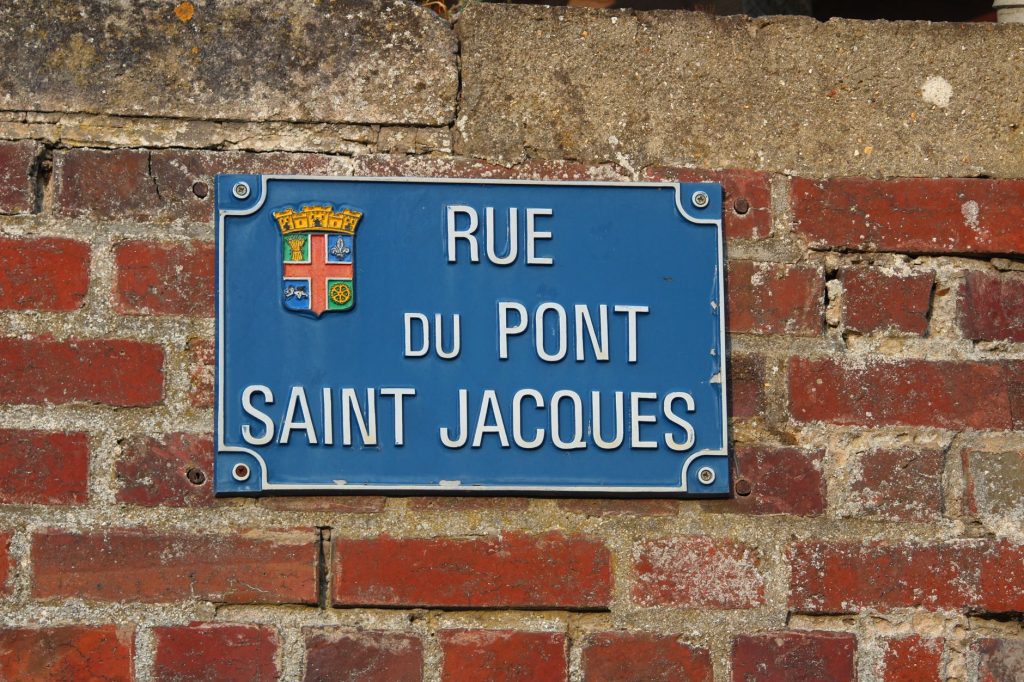 Plaque de rue émaillée bleue fixée sur un mur de brique rouge, signalétique typique des villes du Nord