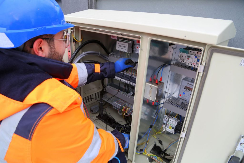 Électricien vérifiant un tableau électrique et ses disjoncteurs lors d'une intervention de dépannage