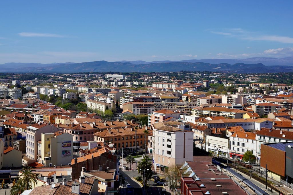 Vue aérienne d'une ville méditerranéenne dominée par des montagnes, sous un ciel dégagé